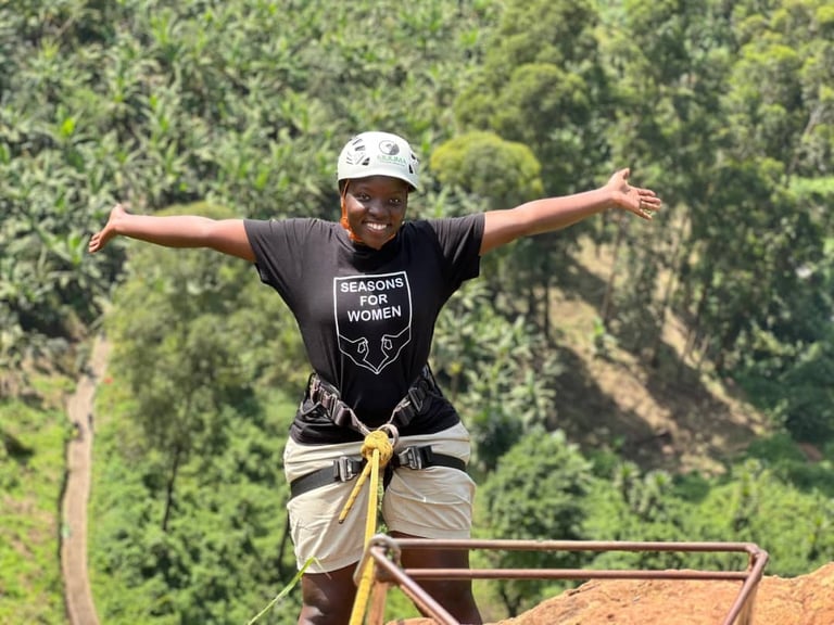 Person wearing a helmet and harness with arms outstretched on a zip line course above a forested valley